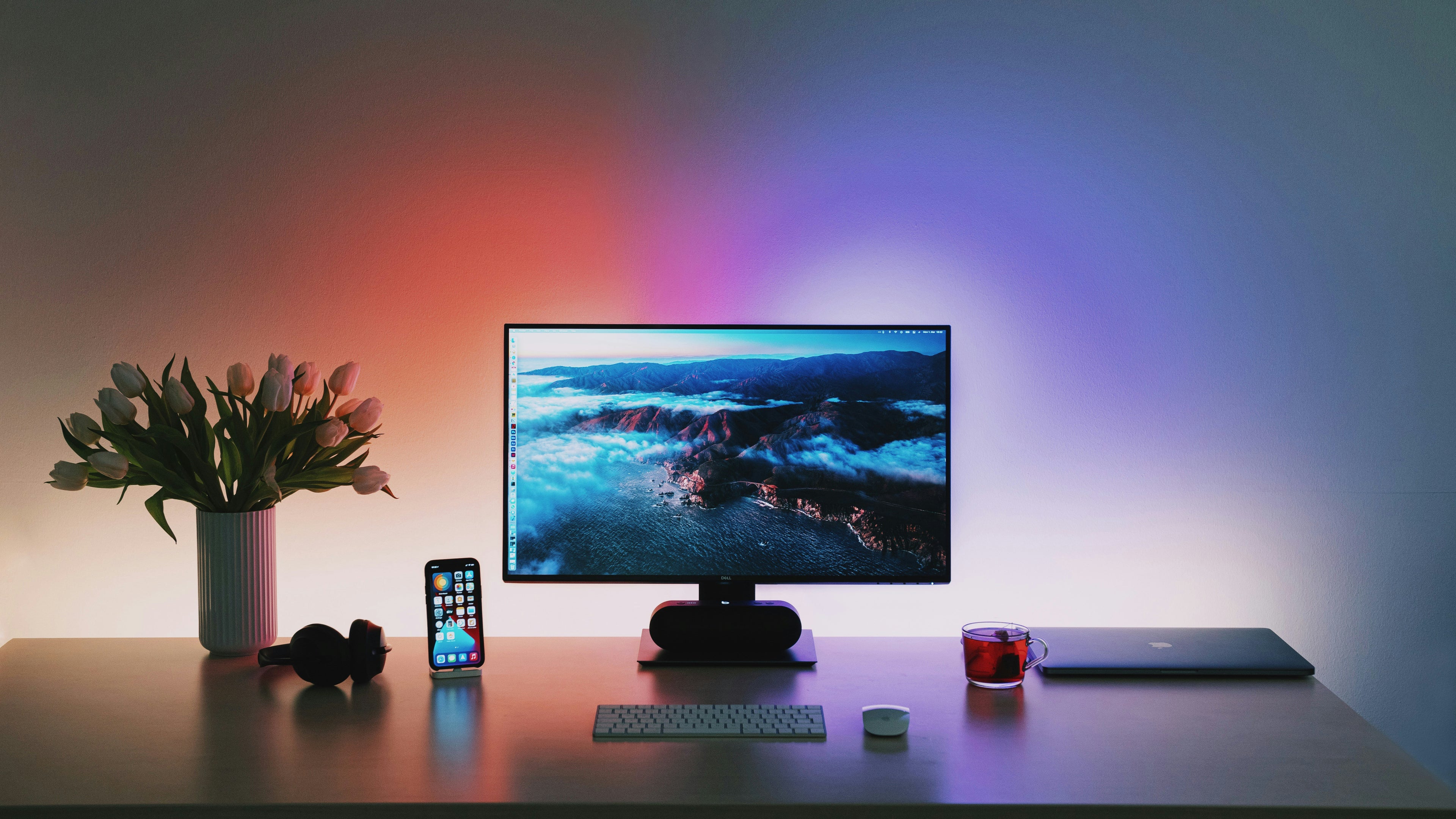 Modern desk setup with computer monitor, phone, and other items against a colorful gradient background