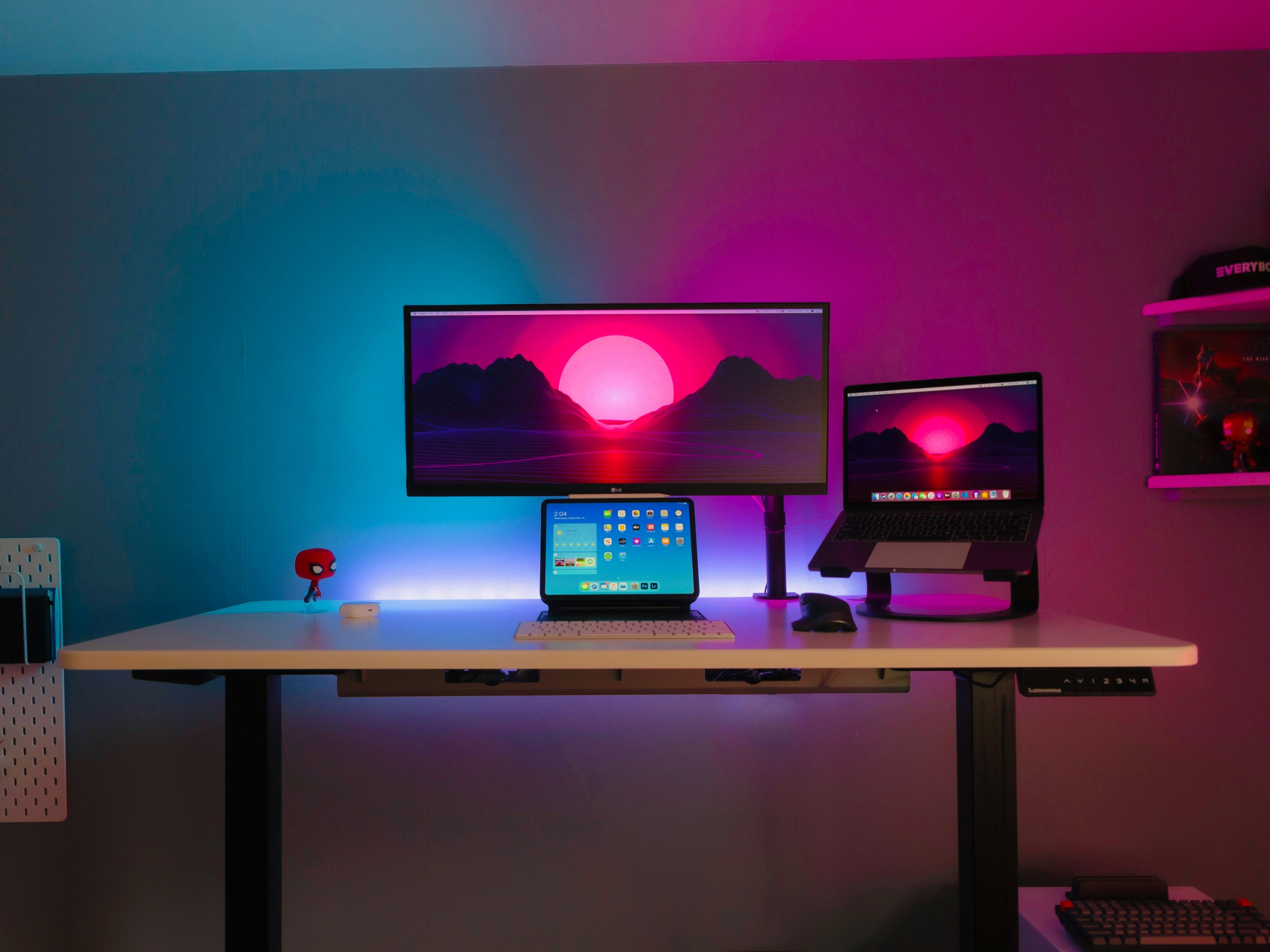 Modern desk setup with multiple monitors and a laptop under colorful LED lights.
